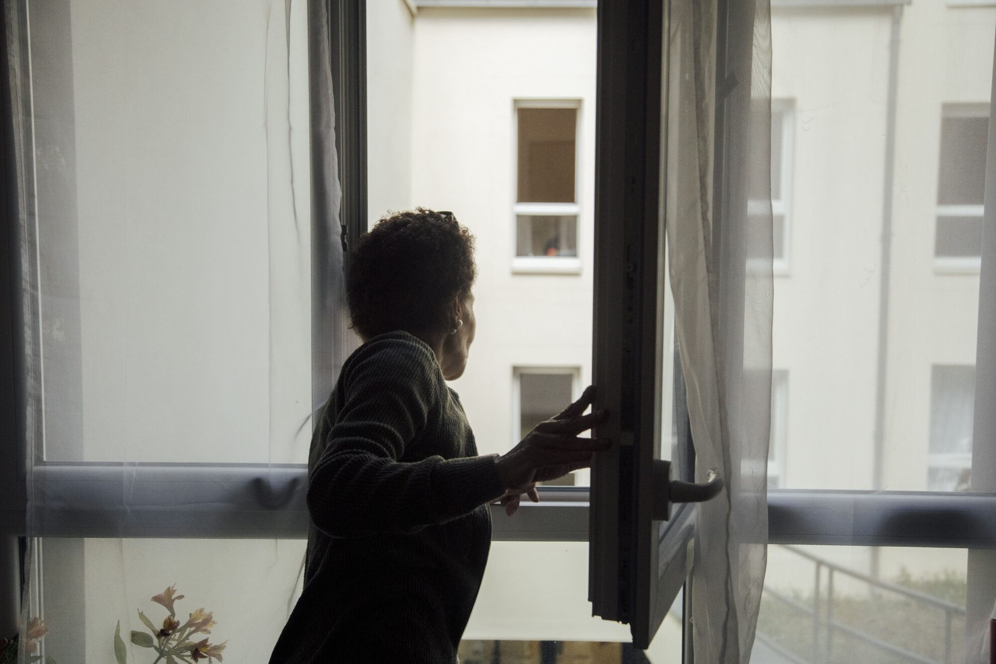 Photo d'une personne âgée ouvrant la fenêtre de son appartement dans un immeuble de banlieue